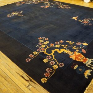 Navy rug with detailed yellow and pink flowering branches and vase motifs displayed on wide wood planks.