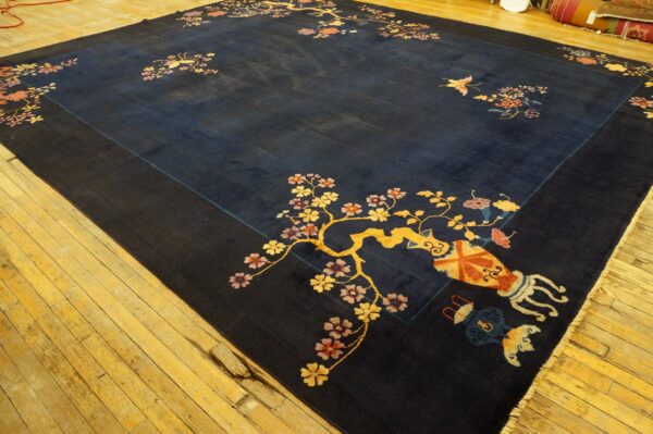 Navy rug with detailed yellow and pink flowering branches and vase motifs displayed on wide wood planks.