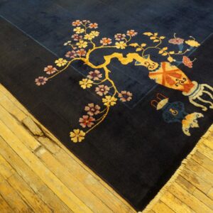 Dark blue rug with a large golden floral vine and patterned vases rests on distressed yellow wood floors.
