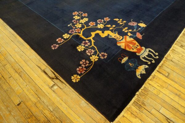 Dark blue rug with a large golden floral vine and patterned vases rests on distressed yellow wood floors.