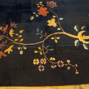 Dark blue rug with a medium pile featuring a gold vine and red, purple, and yellow floral pattern on wood flooring.