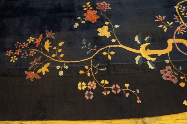 Dark blue rug with a medium pile featuring a gold vine and red, purple, and yellow floral pattern on wood flooring.