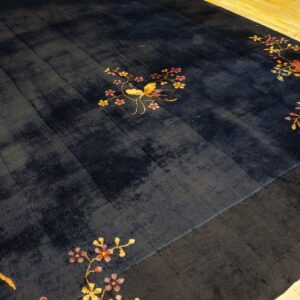 Dark blue rug with gold bird and colorful floral designs on bright wood plank flooring.