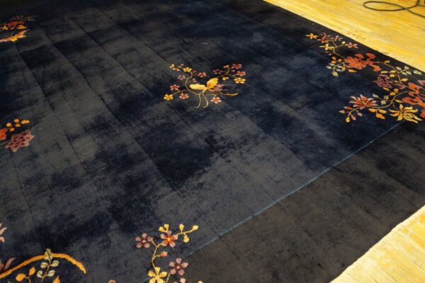 Dark blue rug with gold bird and colorful floral designs on bright wood plank flooring.