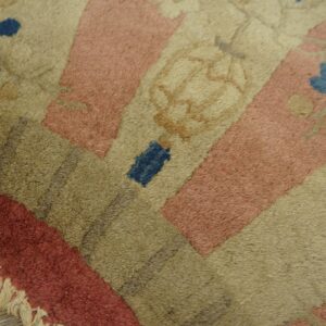 Corner detail of a shaggy pink, tan, and olive rug with blue flowers and fringe on wood flooring.