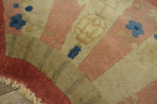 Corner detail of a shaggy pink, tan, and olive rug with blue flowers and fringe on wood flooring.