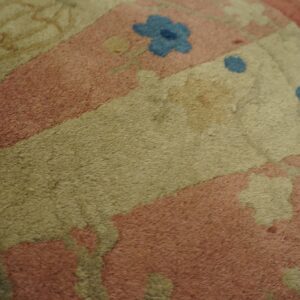 A high-pile rug with a floral pattern in pink, beige, olive, and blue rests on light wood floorboards.