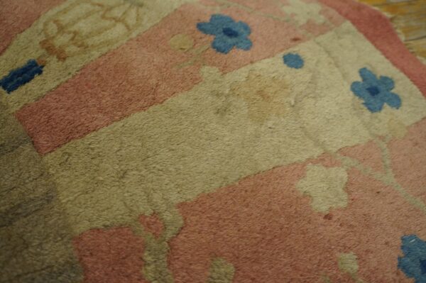 A high-pile rug with a floral pattern in pink, beige, olive, and blue rests on light wood floorboards.