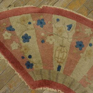A fan-shaped rug in pink and beige with blue floral motifs rests on distressed wood planks.