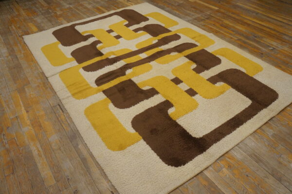 Shag rug in cream, brown, and yellow with a large abstract interlocking pattern on distressed wood flooring.
