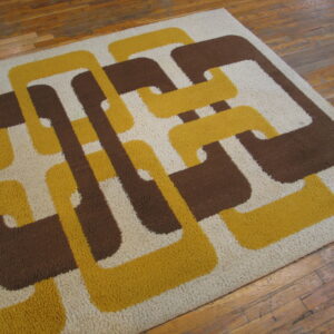 High-pile rug with a retro yellow, brown, and cream interlocking geometric pattern on wood planks.