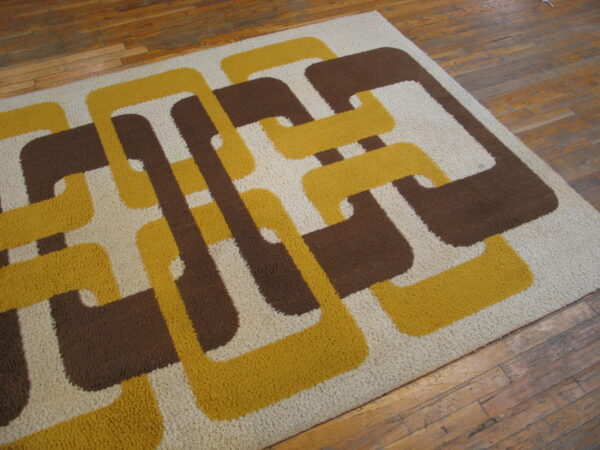 High-pile rug with a retro yellow, brown, and cream interlocking geometric pattern on wood planks.