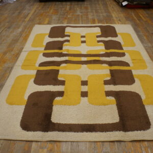 High-pile rug with interlocking geometric shapes in cream, golden yellow, and dark brown on wood flooring.