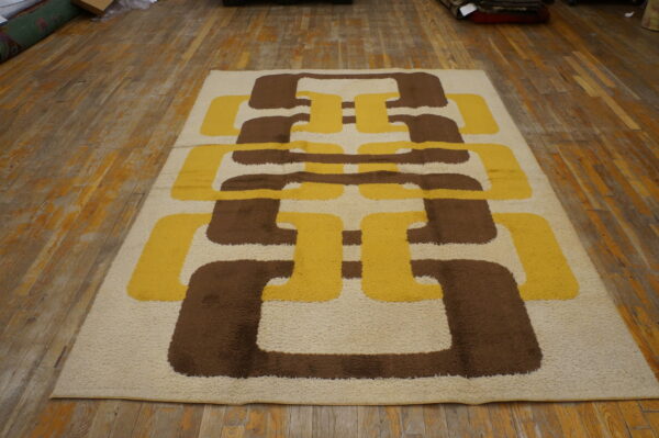 High-pile rug with interlocking geometric shapes in cream, golden yellow, and dark brown on wood flooring.