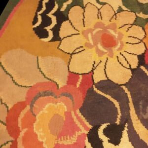 Close-up detail of a round rug showing stylized floral patterns in gold, black, green, and bright pink.