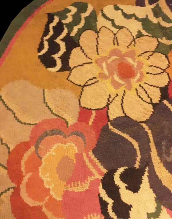 Close-up detail of a round rug showing stylized floral patterns in gold, black, green, and bright pink.