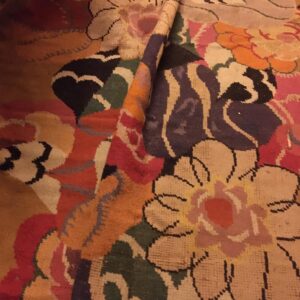 A rolled-up rug displays a colorful, abstract floral design with tan, pink, green, and purple motifs.