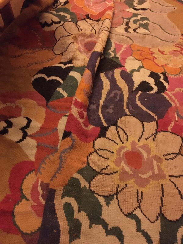 A rolled-up rug displays a colorful, abstract floral design with tan, pink, green, and purple motifs.