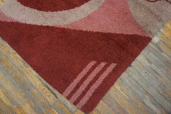 Abstract, shaggy rug with red, pink, and tan curved stripes covers worn wood flooring.