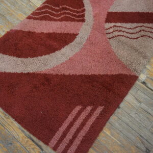 Shaggy maroon, pink, and gray rug featuring curved shapes and wavy lines on distressed wood floor.