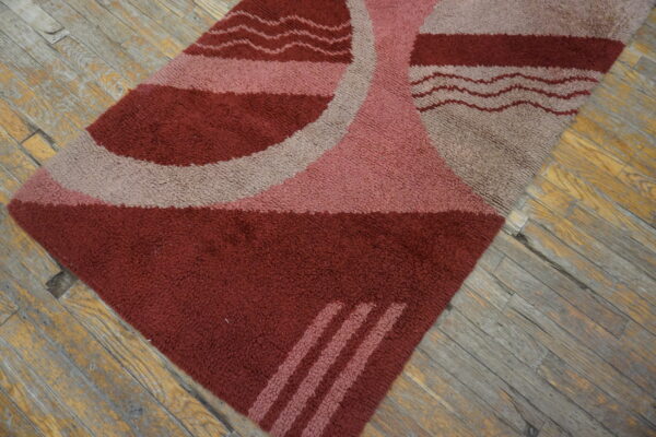 Shaggy maroon, pink, and gray rug featuring curved shapes and wavy lines on distressed wood floor.