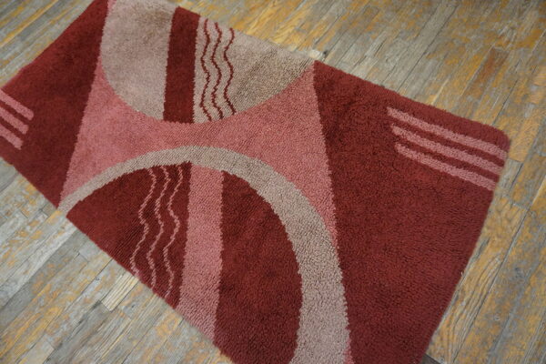A reddish geometric shag rug with tan and pink accents sits on weathered hardwood floors.