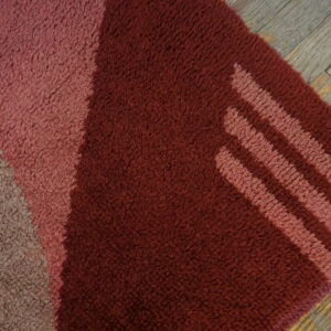 Textured rug featuring blocks of burgundy, pink, and tan with diagonal stripes, set on weathered wood planks.