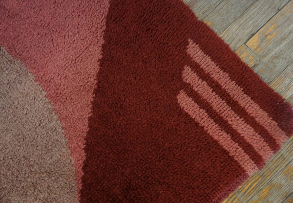 Textured rug featuring blocks of burgundy, pink, and tan with diagonal stripes, set on weathered wood planks.