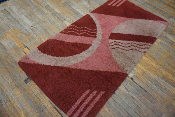High-pile rectangular rug with red, pink, and taupe geometric shapes on distressed wood flooring.
