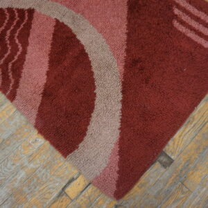 Textured maroon rug with abstract curved shapes in pink and taupe on rustic wood floors.