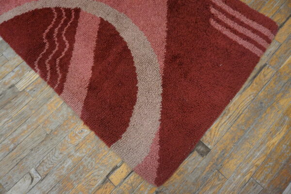 Textured maroon rug with abstract curved shapes in pink and taupe on rustic wood floors.