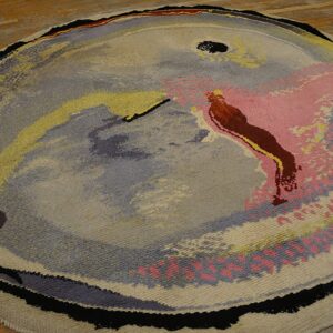 Circular rug featuring a low-pile abstract design in gray, pink, yellow, and brown on hardwood floor.