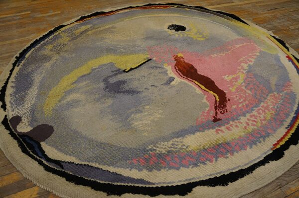 Circular rug featuring a low-pile abstract design in gray, pink, yellow, and brown on hardwood floor.