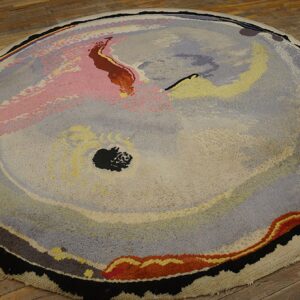 Round abstract rug featuring painterly swaths of pink, gray, yellow, and black on wood plank flooring.