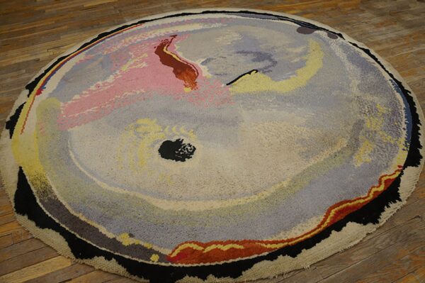 Round abstract rug featuring painterly swaths of pink, gray, yellow, and black on wood plank flooring.