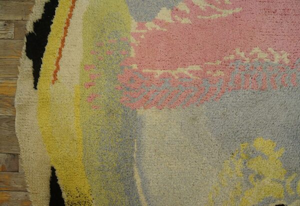 Close-up of a high-pile rug featuring large abstract forms in pink, blue, yellow, and black over wood planks.