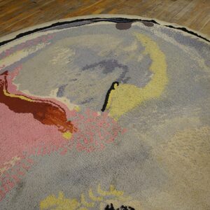 Textured round rug features abstract pink, yellow, gray, and lavender designs on distressed wood plank flooring.