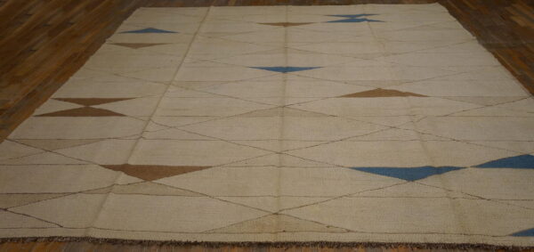 Cream flatwoven rug featuring a geometric pattern of thin intersecting lines and blue and brown triangles on wood flooring.