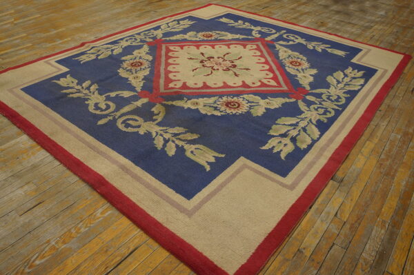 Blue rug featuring a large central beige and red floral design, lying on rustic wood plank flooring.