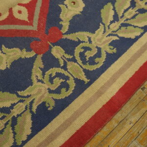 Low-pile rug detail showing blue, red, and sage foliate patterns, striped border, and distressed wood floor.