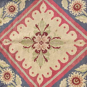 Blue rug detail showing a cream scalloped diamond surrounded by red, sage, and burgundy floral garlands.