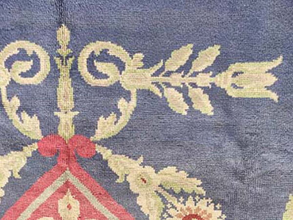 Textured blue rug featuring ornate floral scrollwork in beige, pale green, and salmon pink.