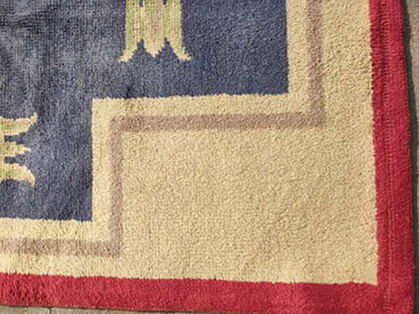 High pile rug corner featuring borders in red, light beige, and taupe surrounding a navy blue field.