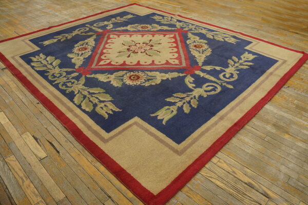 Blue and beige area rug with a detailed red and green floral pattern rests on rustic wood flooring.