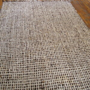 A cream and dark brown open-weave rug with tassels lies on polished wood flooring.