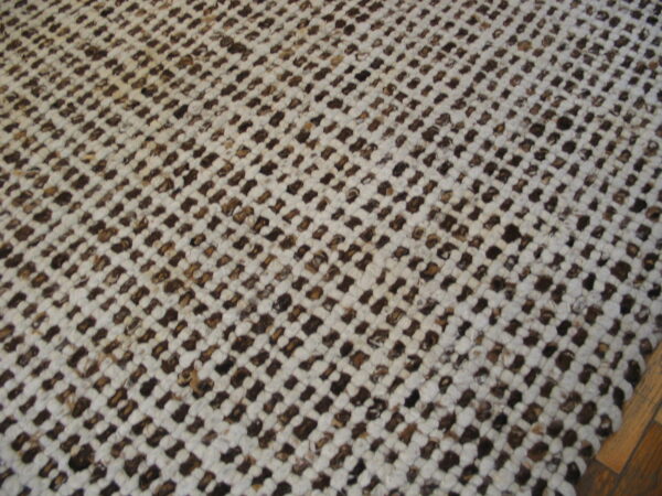 Low-pile textured rug in white and brown woven in a dense, diagonal grid over wood flooring.