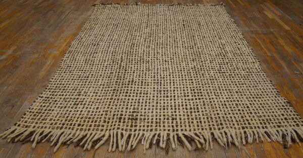 Loosely woven cream and dark brown square-patterned rug with heavy fringe on wood floors.