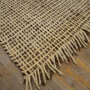 A cream and dark brown open-weave rug with tassels lies on polished wood flooring.