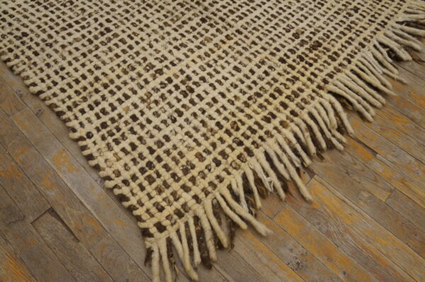 A cream and dark brown open-weave rug with tassels lies on polished wood flooring.