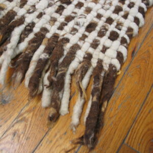 A chunky brown and cream woven rug with thick fringe rests on a warm plank wood floor.